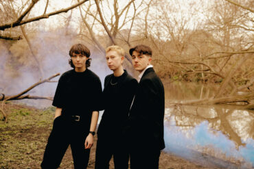 The three members of the band headboy standing beside a river