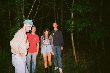 The four members of the band Hotline TNT standing in the woods in the dark