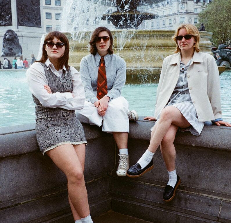 Girl Ray sitting on a wall wearing sunglasses.