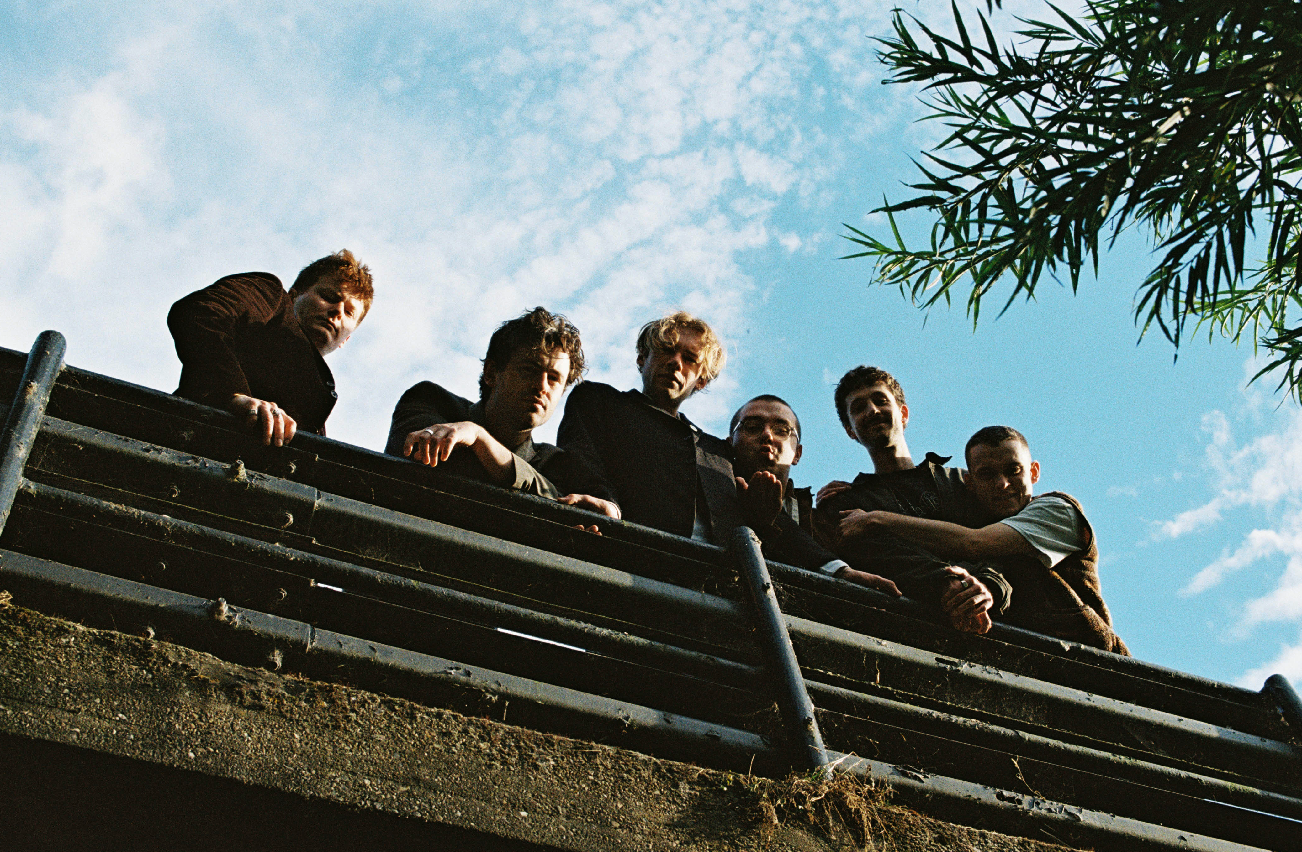 The six members of the band Flat Party looking down into the camera from a bridge