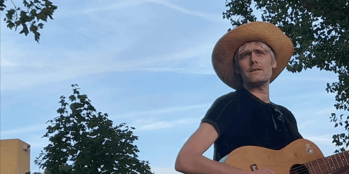 Alex Sebley from Pregoblin wearing a straw hat and holding a guitar.